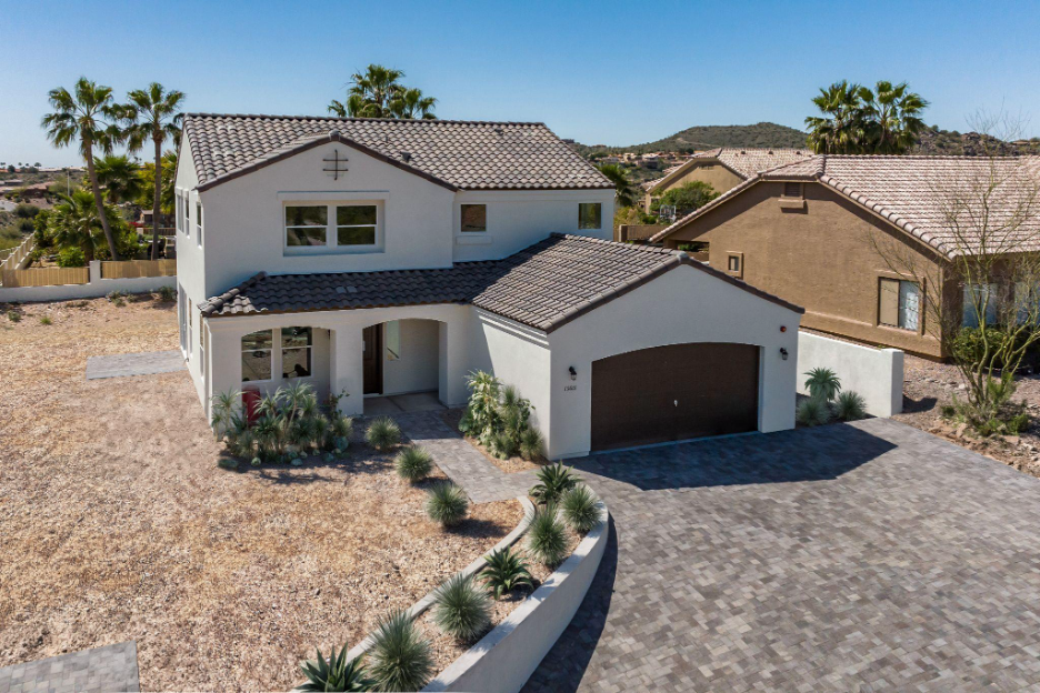 Newly constructed two-story Adair home in Arizona, featuring a stucco exterior, tile roof, desert landscaping, and a paver driveway in a residential neighborhood.