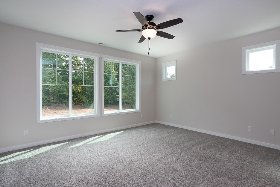 Bright bedroom with large picture windows, soft carpeting, and a ceiling fan, showcasing natural light and a serene outdoor view.