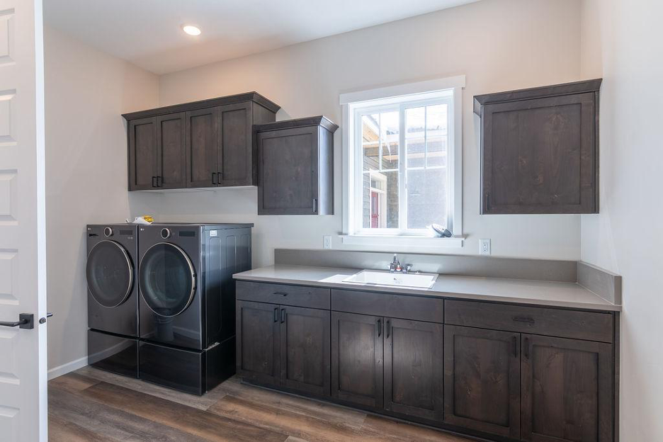 Laundry room with dark wood cabinets, a deep utility sink, and modern front-loading washer and dryer beneath a bright window.