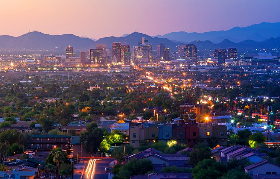 Panoramic view of downtown Phoenix, Arizona at sunset with city lights, desert landscape, and surrounding mountain ranges.