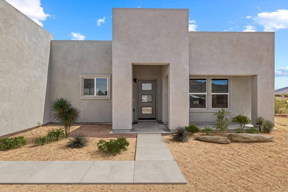 Contemporary flat-roof home with clean stucco design, desert plants, and a concrete walkway leading to the front entrance.