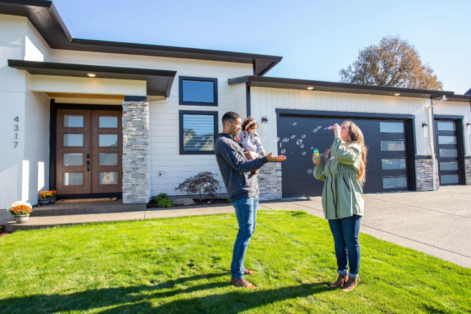 A family playing with bubbles on the front lawn of their newly built modern Adair custom home, showcasing a stone-accented entryway and large garage.