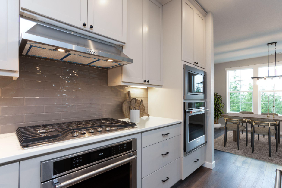 Bright, contemporary kitchen with built-in stainless steel appliances, a gas cooktop, white cabinetry, and a view into a dining space with natural light.
