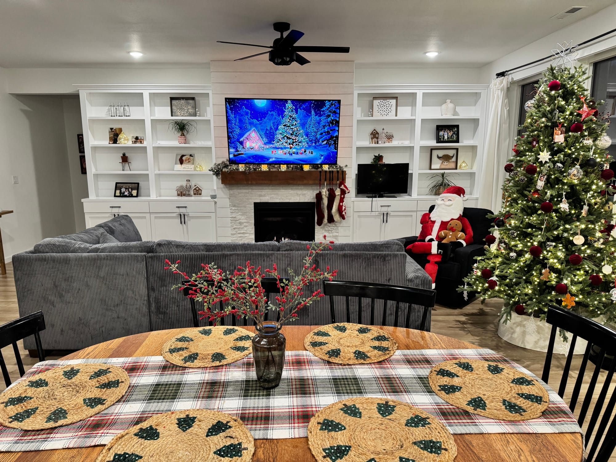 Living room with built-ins, a Christmas tree, fireplace, and a dining table decorated for the holidays.