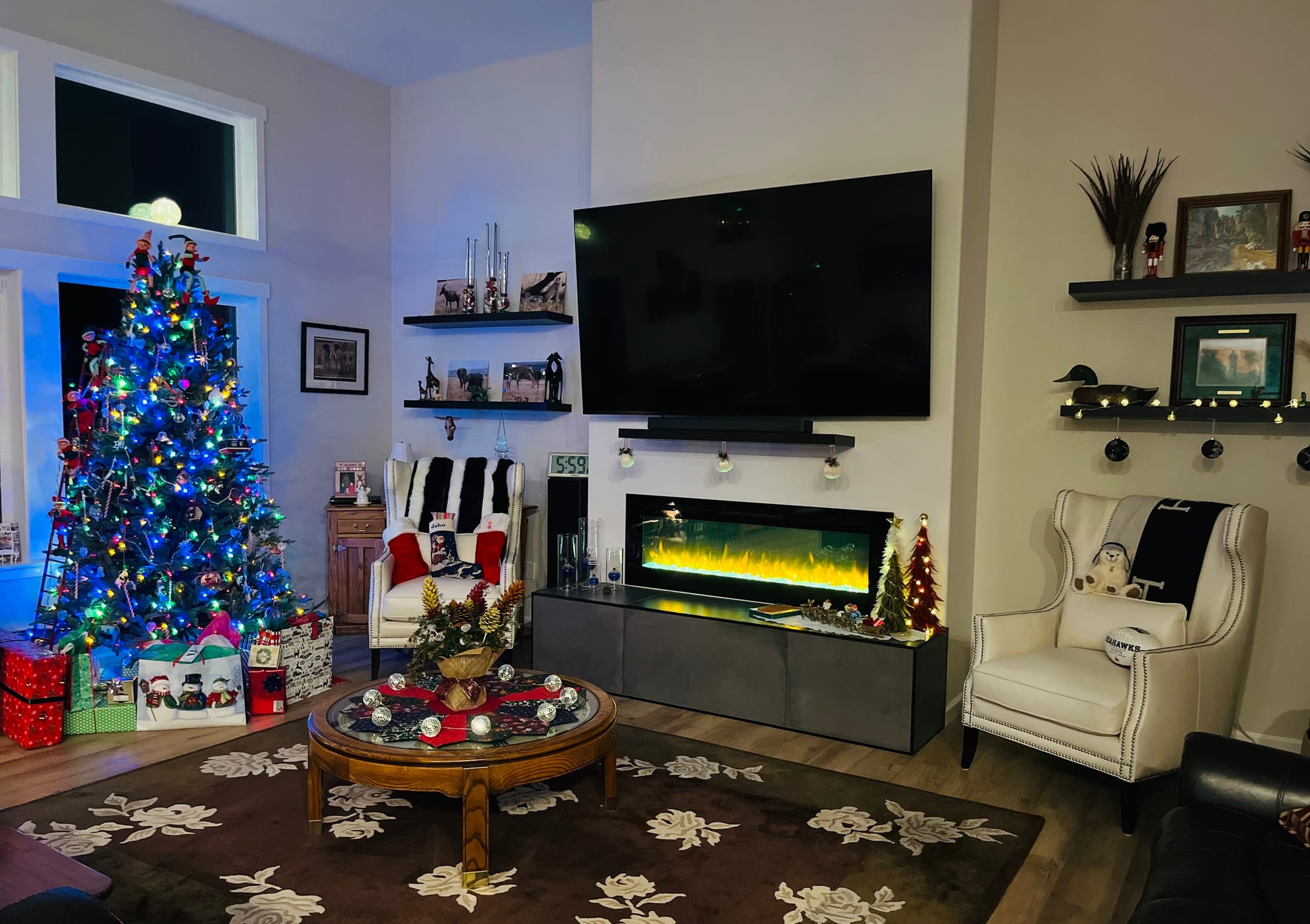 Cozy room with a lit Christmas tree, modern fireplace, wall-mounted TV, and holiday décor.