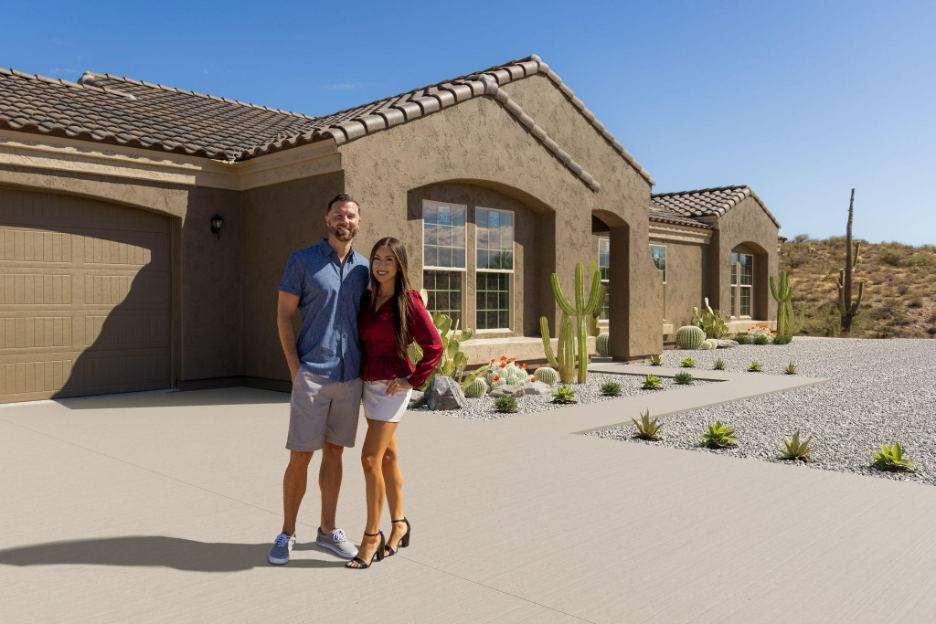 A couple standing in front of a stucco home surrounded by desert landscaping and cacti.