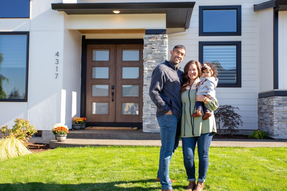 Happy family standing in front of their newly built modern custom home with landscaped yard and contemporary front entry.