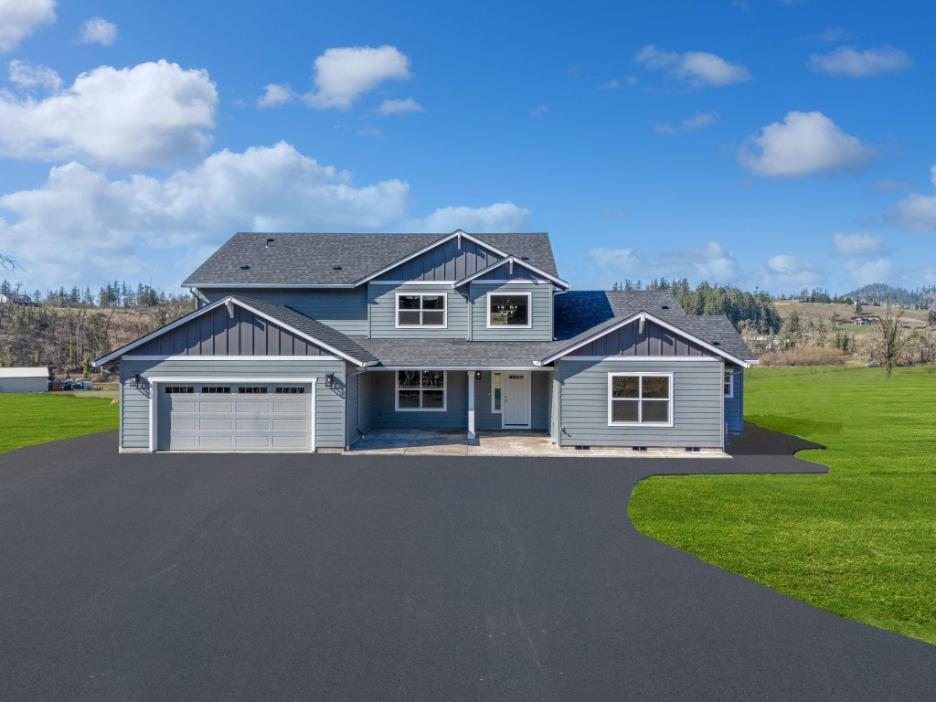 Newly built two-story custom home with blue-gray siding, attached garage, and rural Oregon landscape.