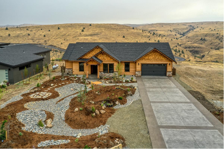 Ranch-style custom home with wood exterior, landscaped front yard, and rolling hillside backdrop.