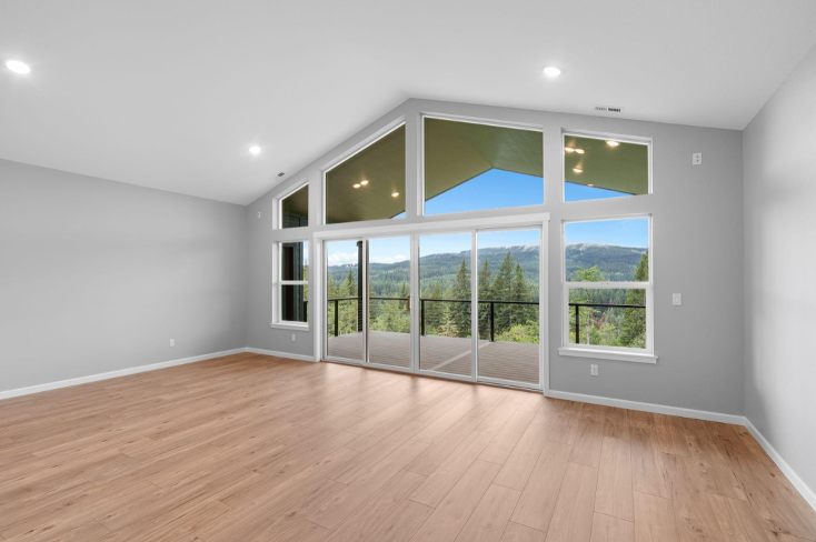 Living room with vaulted ceiling, large picture windows, hardwood floors, and scenic outdoor views.