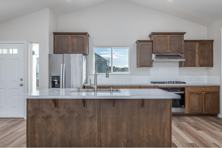 Custom kitchen featuring oversized island, wood cabinetry, stainless appliances, and bright natural light.