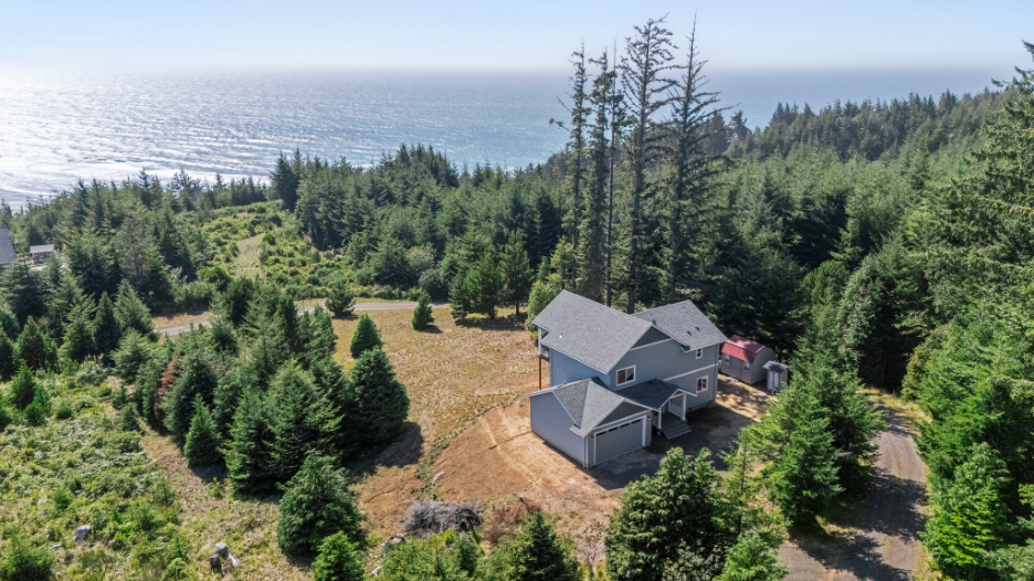 Aerial view of a custom home surrounded by evergreen trees near the Washington coastline and ocean.