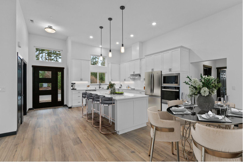 Bright open-concept kitchen with white cabinets, large island, pendant lighting, wood floors, and dining area in a custom home.