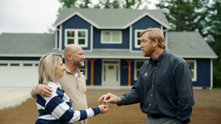Homeowners receiving house keys from a builder in front of a newly completed blue two story home.