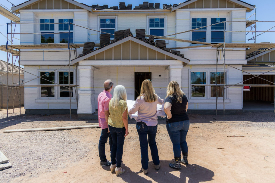 Family reviewing home construction plans in front of a two story house under construction with scaffolding.