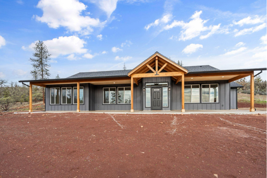 Newly completed single story home with covered front porch, wood beams, and wide driveway on a spacious lot.