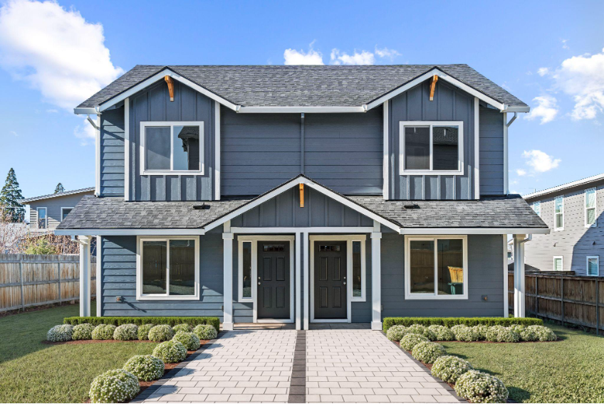 Newly built blue duplex with symmetrical entrances, landscaped front yard, and paved walkway.