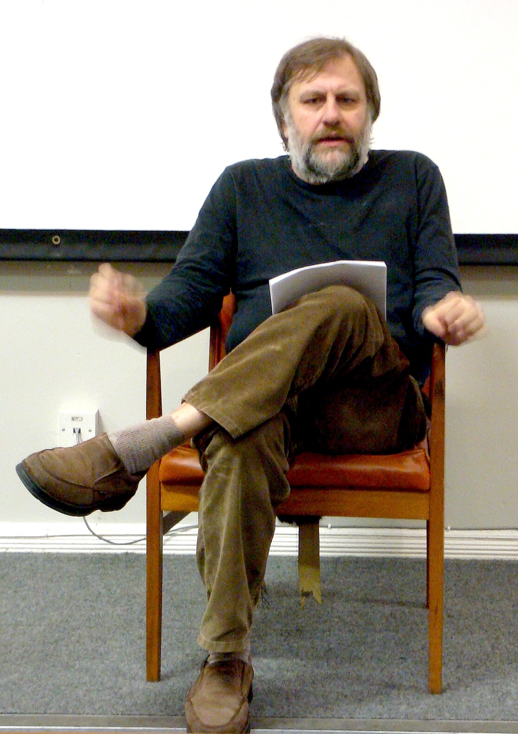 A candid shot of Slavoj Žižek in a chair during a lecture.