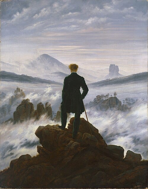 A man in a dark coat stands on a rocky outcrop with his back to the viewer, leaning on a walking stick, gazing across a landscape of mountain peaks emerging from a sea of fog.