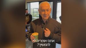 An older man, Israeli Prime Minister Benjamin Netanyahu, stands in what appears to be a café, holding a small coffee cup and looking at the camera. Hebrew text is overlaid on the image. Other patrons are visible blurred in the background.