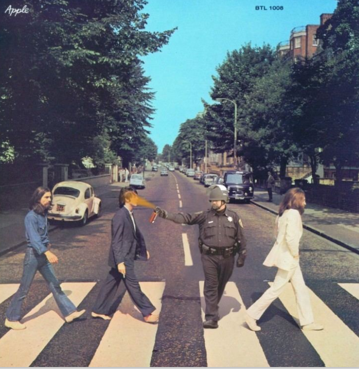 A altered version of the Beatles' Abbey Road album cover. The four figures cross the zebra crossing as in the original, but a uniformed police officer has been inserted among them, pepper-spraying one of the walkers at close range.