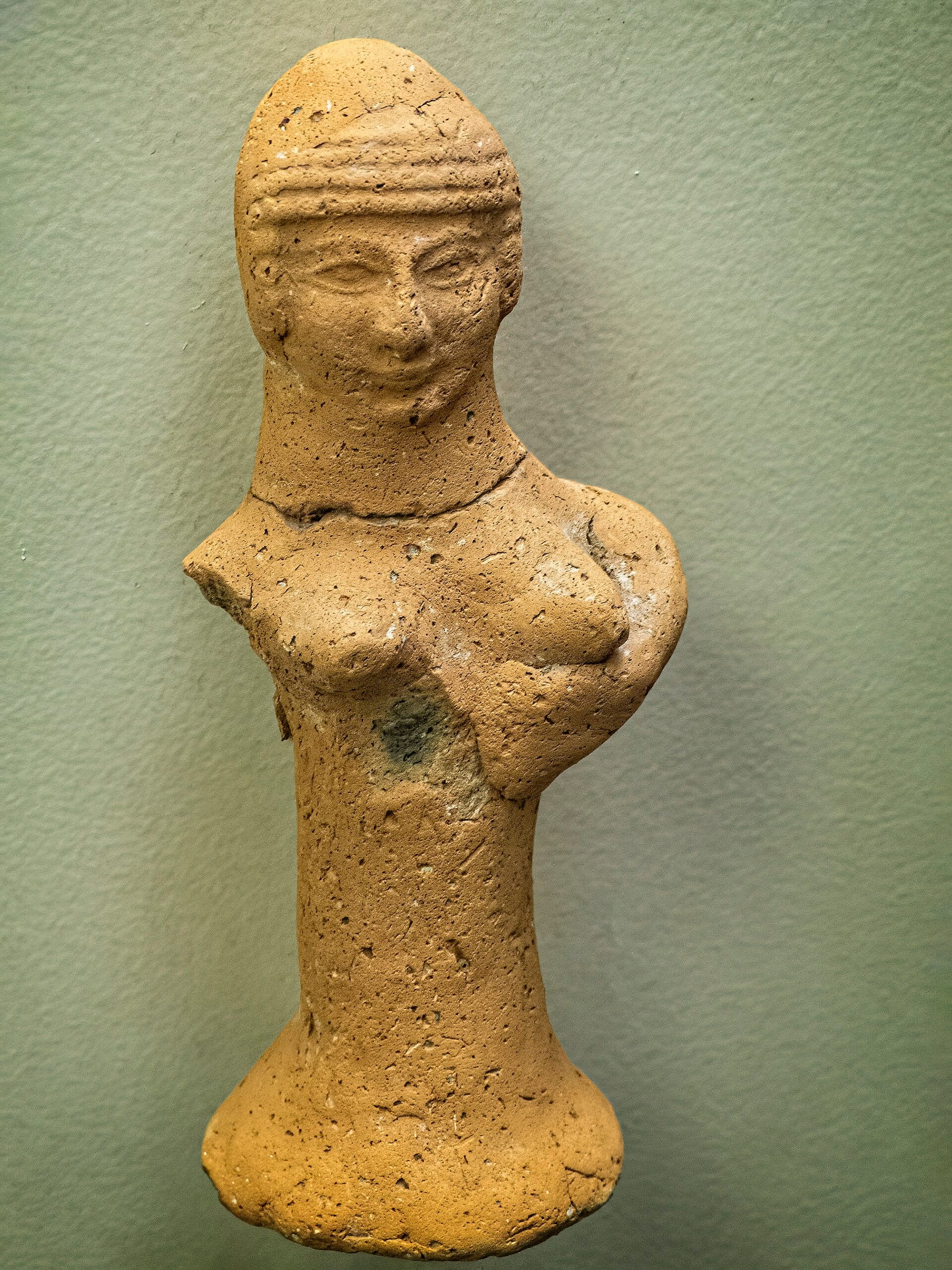 Small terracotta figurine of a woman with hands supporting her breasts on a flaring pillar-shaped base, an Iron Age Judean pillar figurine associated with household worship of a goddess.