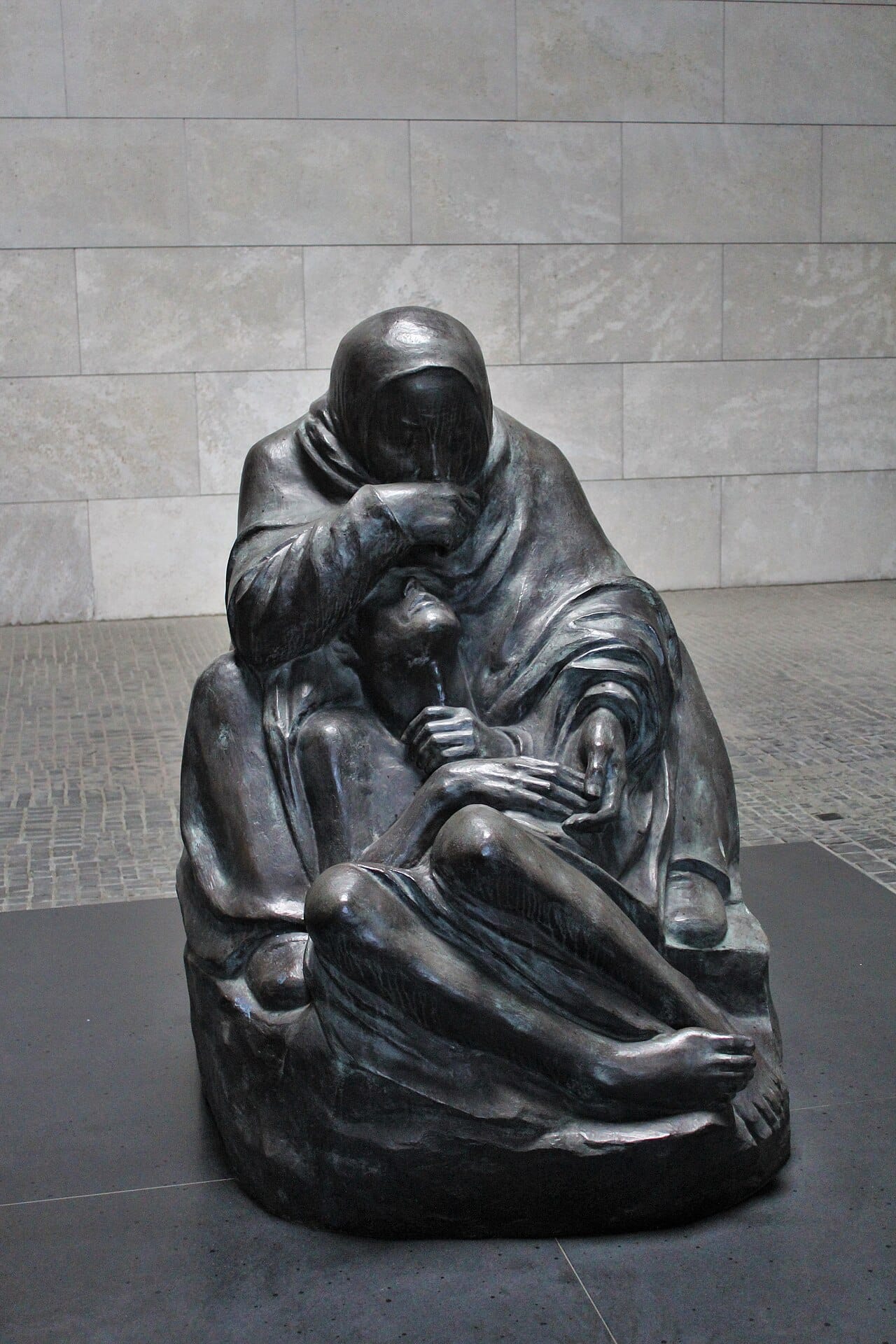  Kollwitz sculpture of a seated mother bowed over the body of her dead son cradled between her knees.