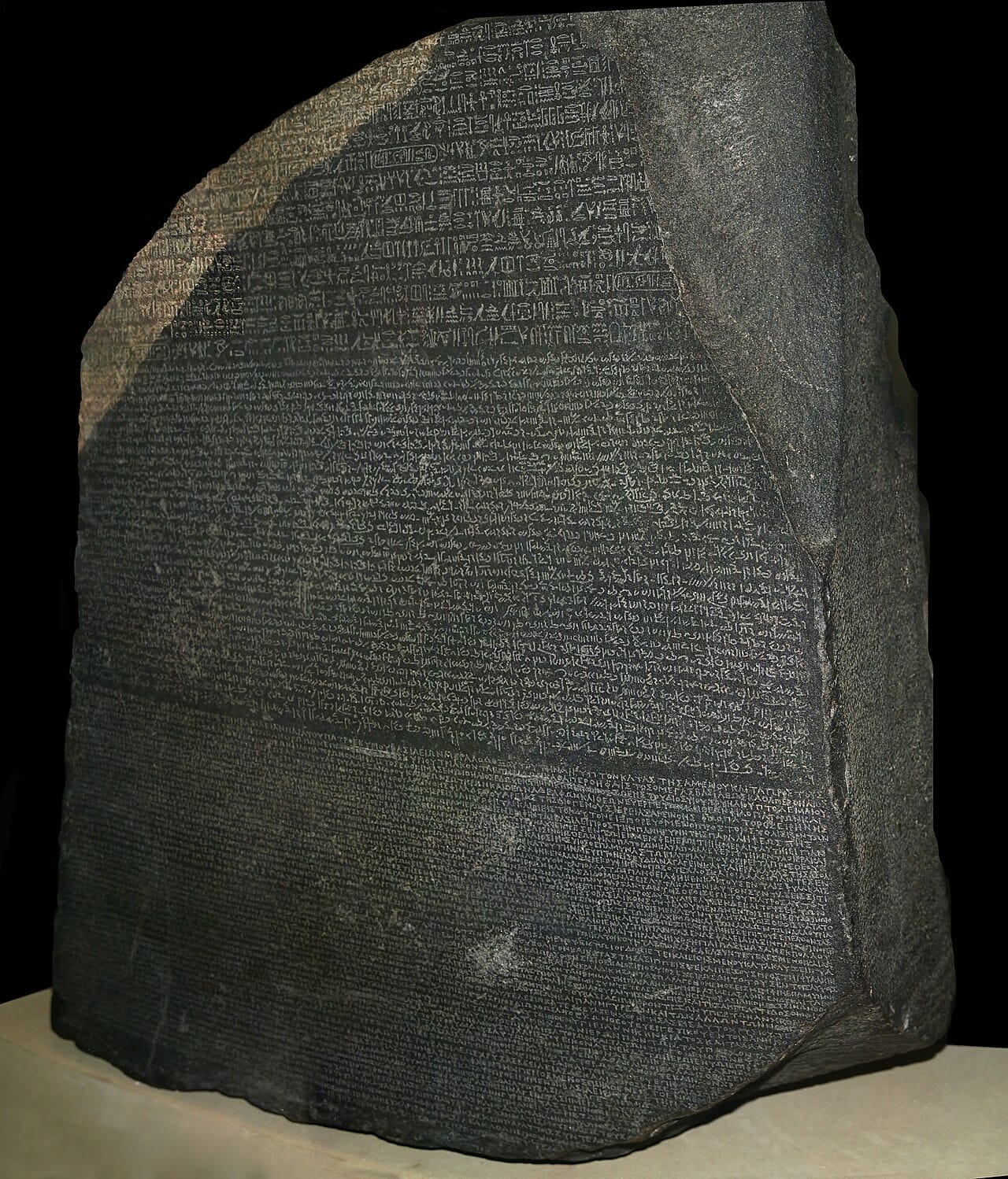 The Rosetta Stone, a dark granite slab densely inscribed in three bands of script: hieroglyphic at the top, Demotic in the middle, Greek below.