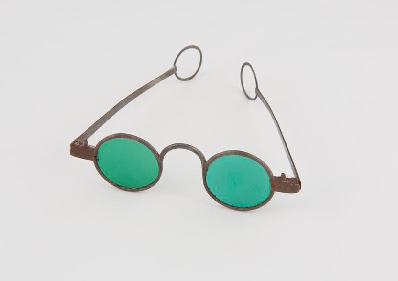 A pair of small eighteenth-century metal-framed spectacles with round green glass lenses, the side arms folded.