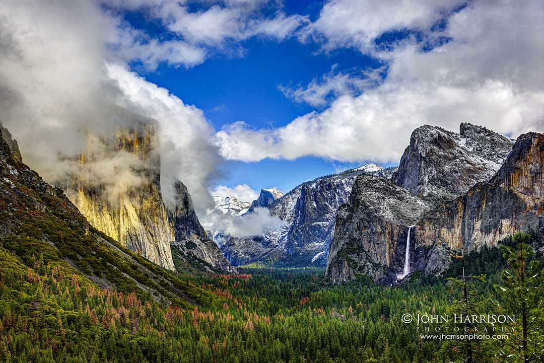 Winter panorama from Tunnel View in Yosemite National Park showing El Capitan, Half Dome, and Bridalveil Fall with snow-dusted granite cliffs and low clouds drifting through Yosemite Valley.