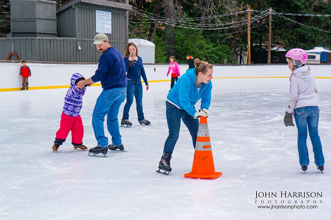 Family ice skating at the Curry Village ice rink in Yosemite National Park during winter, with kids learning to skate and visitors enjoying the outdoor rink.