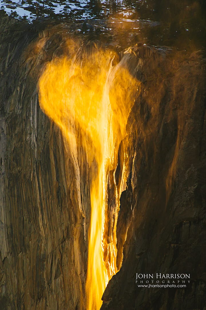 A vertical fine art photograph of the Yosemite Firefall where a rare gust of wind has shaped the glowing orange mist into a distinct heart shape against the dark granite cliff of El Capitan at sunset.