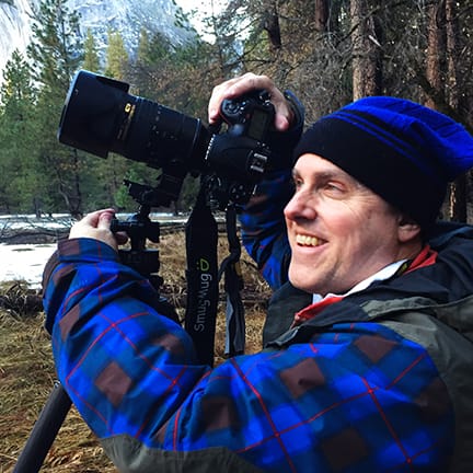 A landscape photographer using a Nikon DSLR on a Gitzo tripod while capturing winter scenery in Yosemite National Park, we