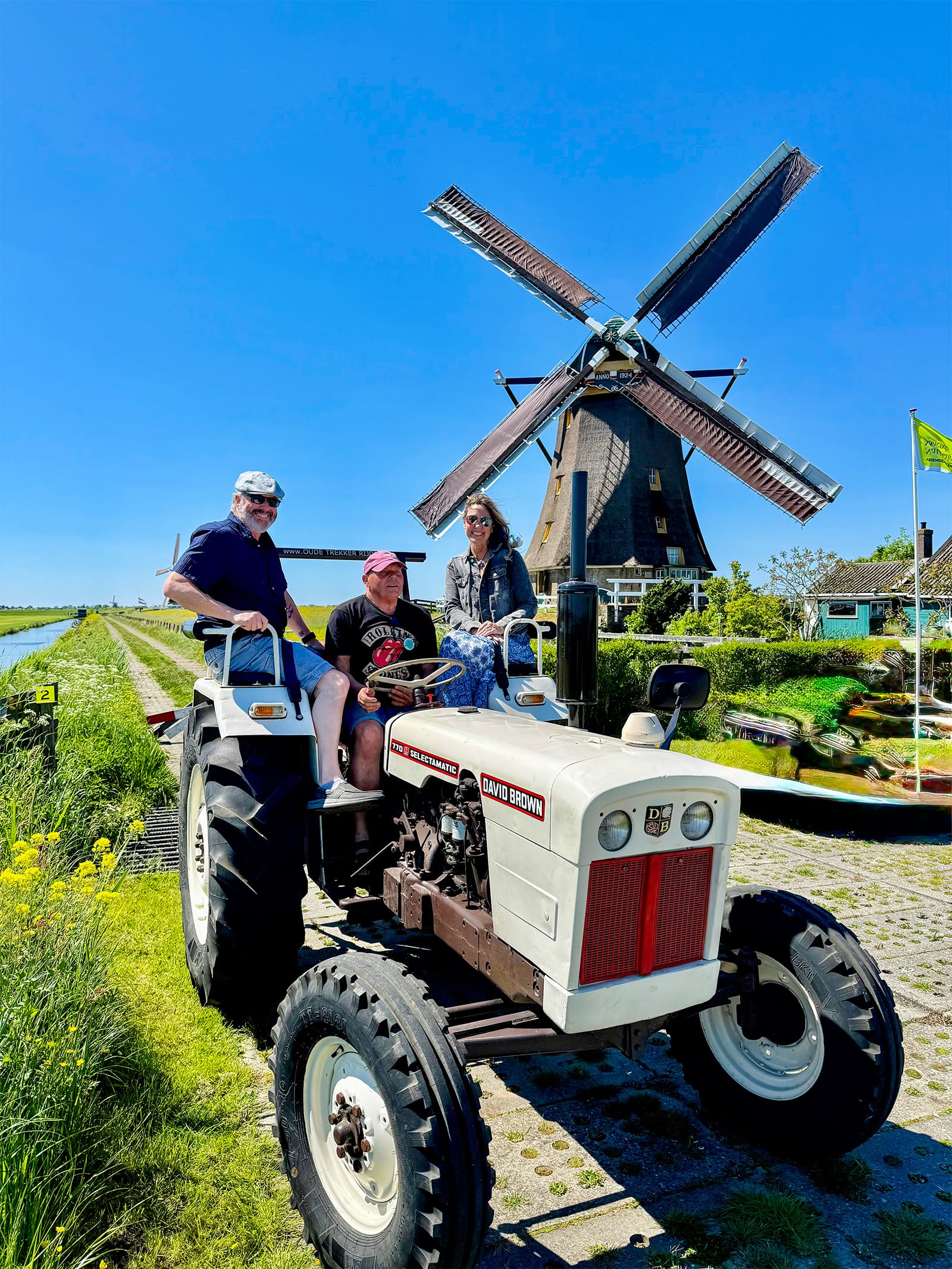 Visitors riding a tractor near Aarlanderveen windmills in the Netherlands with traditional Dutch polder landscape and working windmill in background