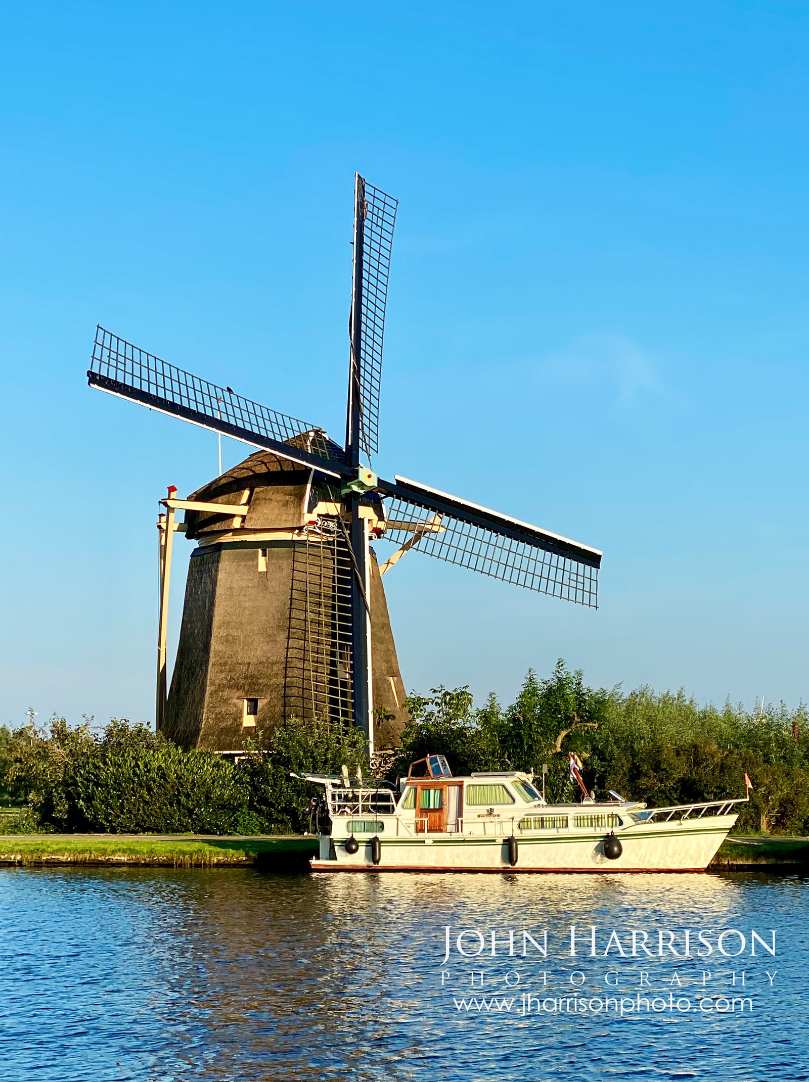 De Zwaan windmill beside the Amstel River near Ouderkerk aan de Amstel in North Holland, Netherlands, photographed during golden summer evening light with a Dutch boat passing by.