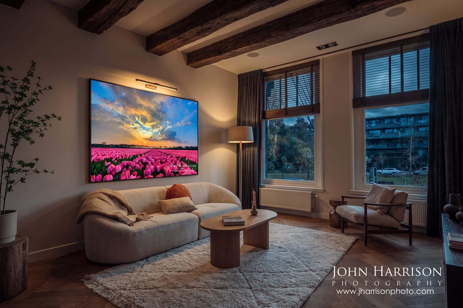 Framed fine art photograph of pink tulip fields displayed in a modern living room interior with soft lighting, neutral tones, and cozy seating.