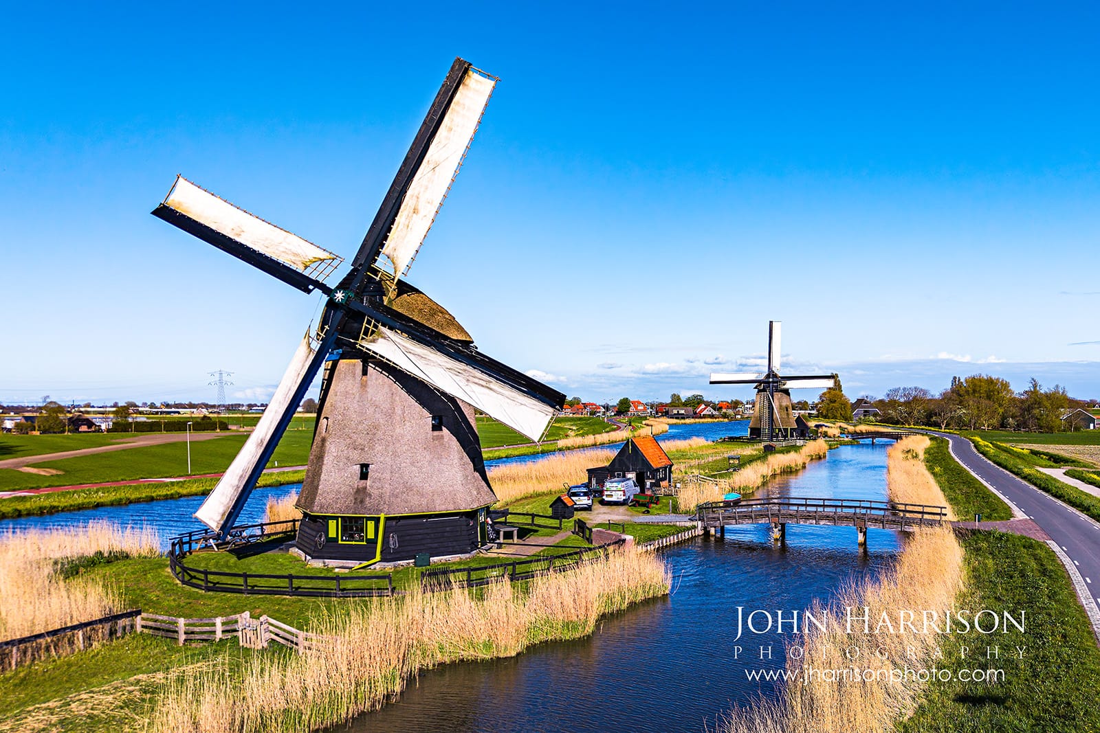 Two Dutch windmills with sails turning along a canal in the Schermer polder near Ursem and Oterleek in North Holland Netherlands