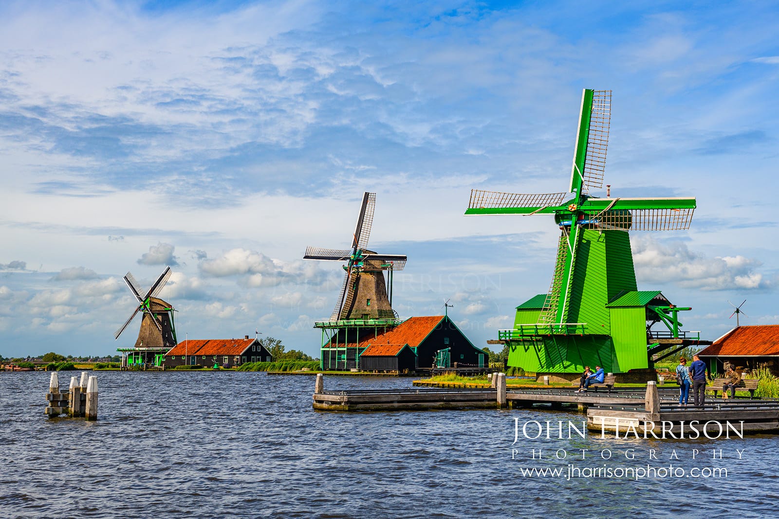 Three traditional Dutch windmills De Kat De Zoeker and Het Jonge Schaap at Zaanse Schans along the Zaan River in the Netherlands on a bright day