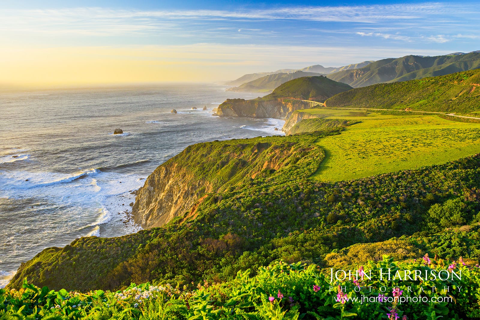 Bixby Bridge at sunrise in Big Sur California with coastal fog flowing through Bixby Creek Canyon and warm morning light illuminating the cliffs.