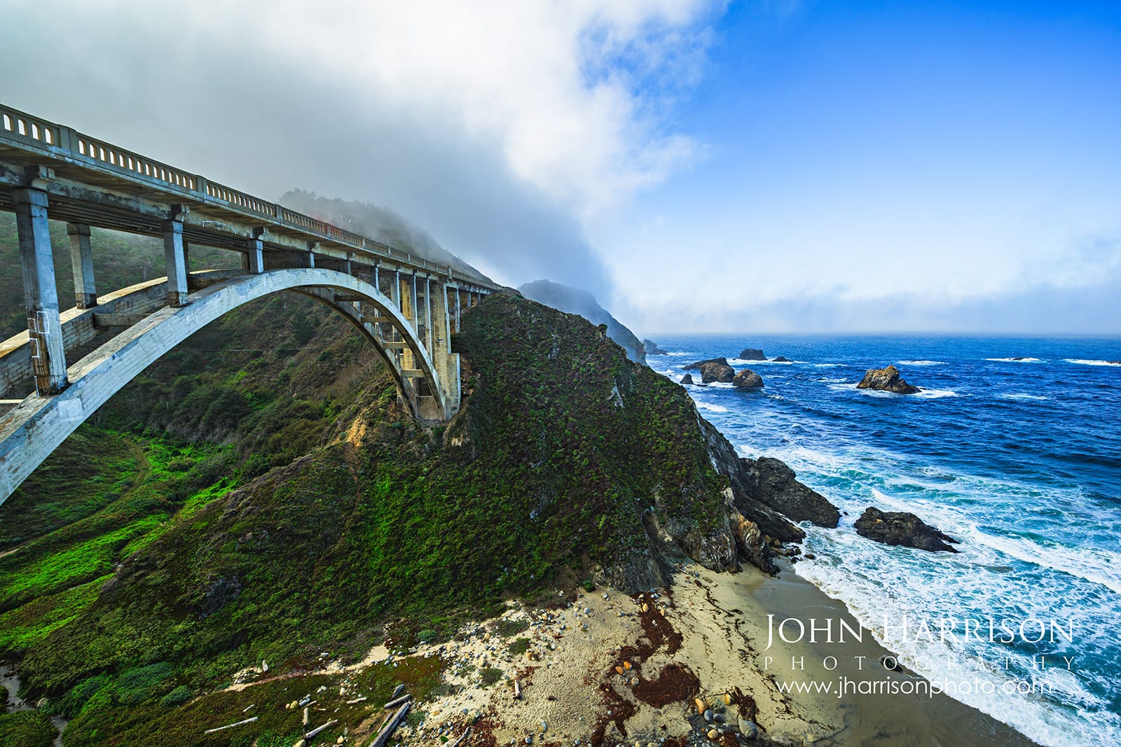 Bixby Bridge along California's Big Sur coast with coastal fog, Pacific Ocean waves, rugged cliffs, and Highway 1 crossing Bixby Creek Canyon.
