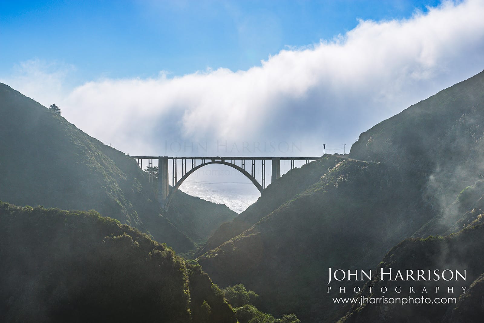 Bixby Bridge in Big Sur California emerging from coastal fog as marine clouds roll over the hills above Bixby Creek Canyon.