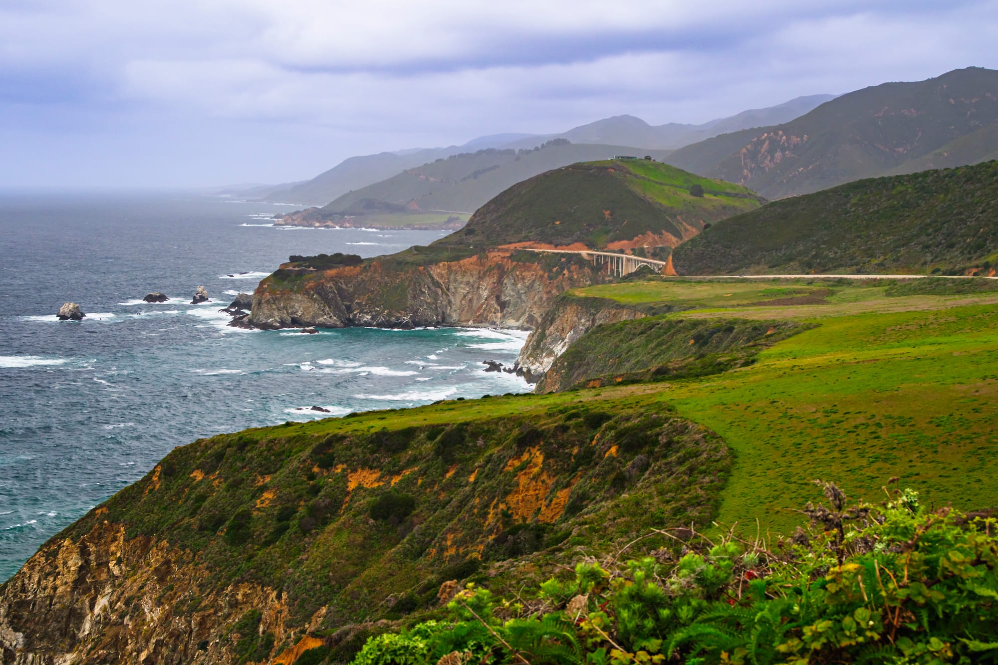 Bixby Creek Bridge surrounded by coastal fog and rolling green hills along Highway 1 near Big Sur California.