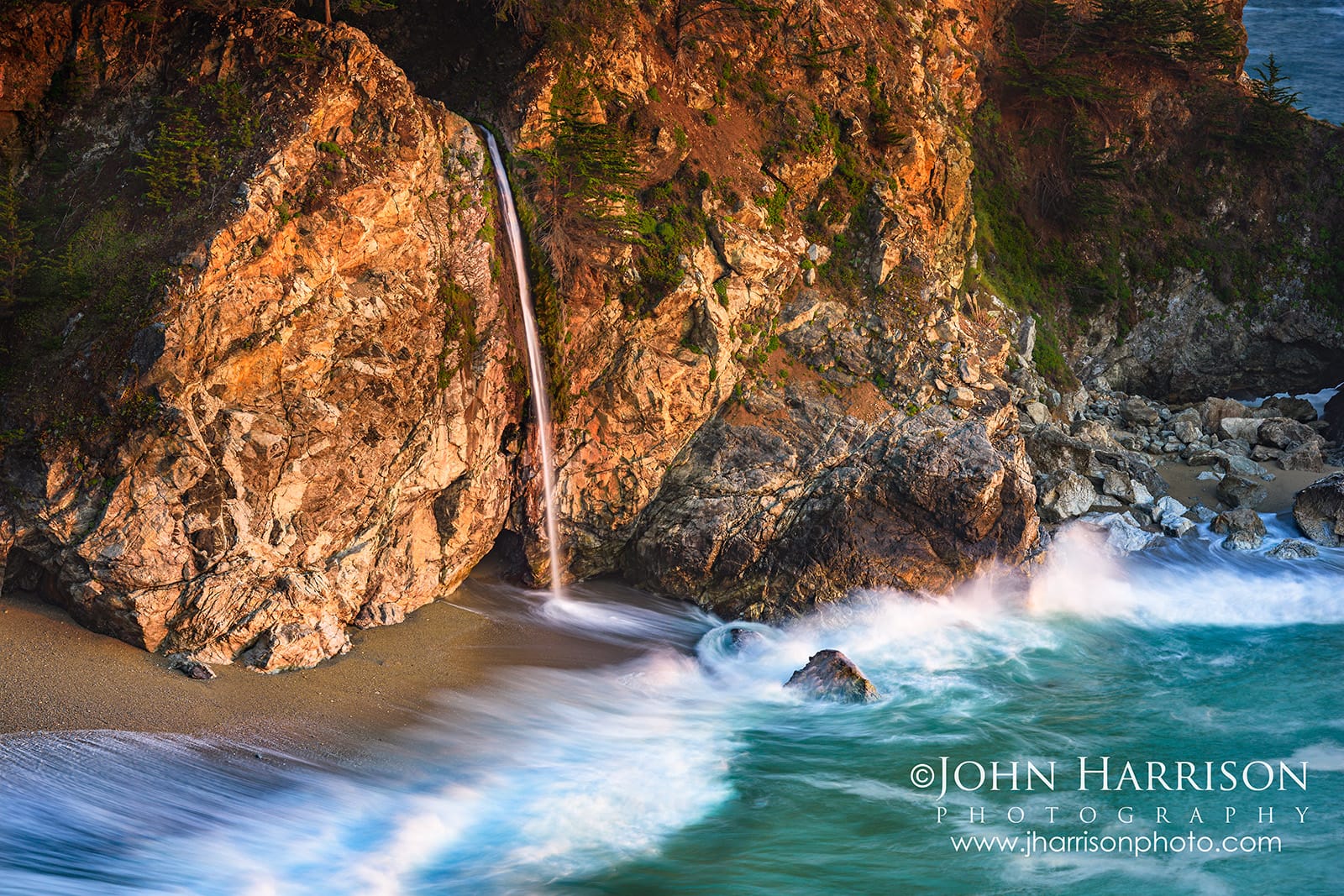 Close-up photograph of McWay Falls flowing into the Pacific Ocean at sunset in Big Sur, California, with golden cliffs, turquoise water, and blurred waves from a long exposure.