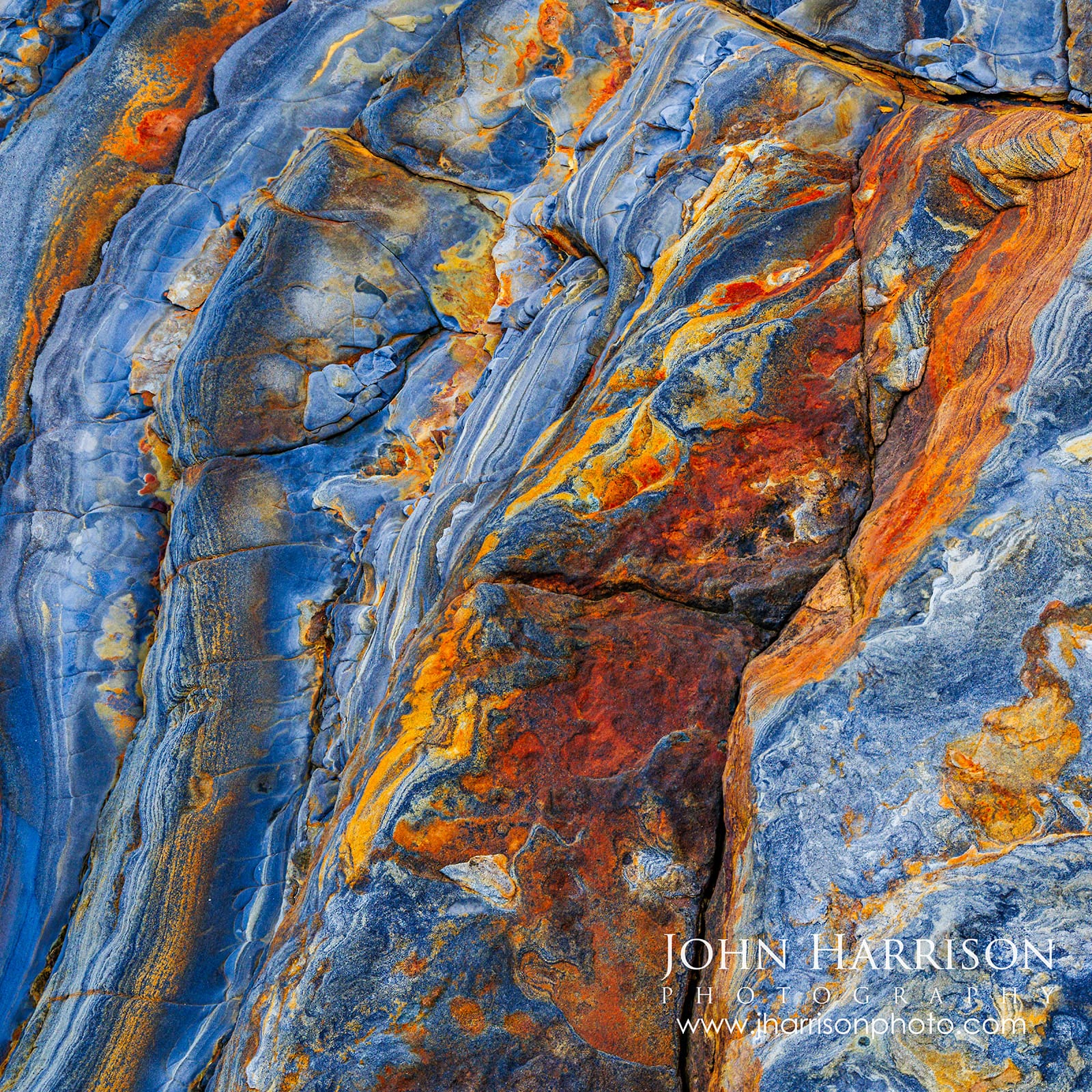 Square abstract photograph of naturally colored blue, rust, orange and gold rock textures at Weston Beach in Point Lobos State Natural Reserve, California.