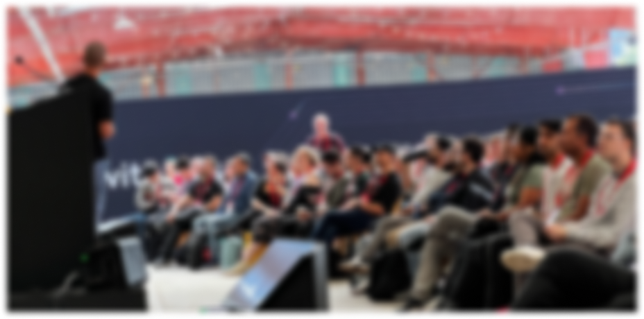 A crowd of people look towards a stage where a presenter is giving a talk