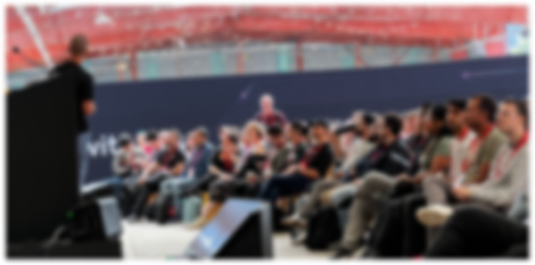 A crowd of people look towards a stage where a presenter is giving a talk