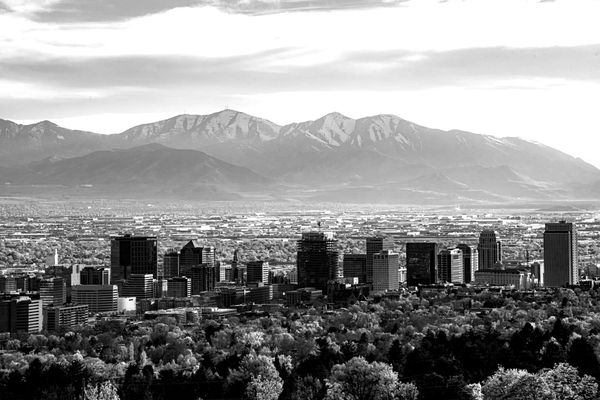 Aerial view of the Salt Lake City skyline with downtown skyscrapers, tree-lined neighborhoods, and the snow-capped Wasatch Mountains in the background