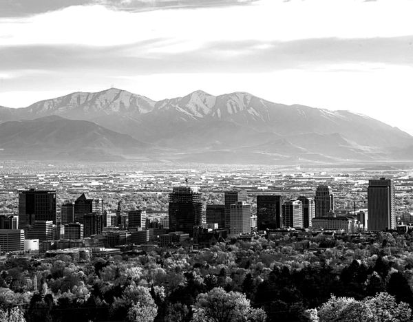 Aerial view of the Salt Lake City skyline with downtown skyscrapers, tree-lined neighborhoods, and the snow-capped Wasatch Mountains in the background