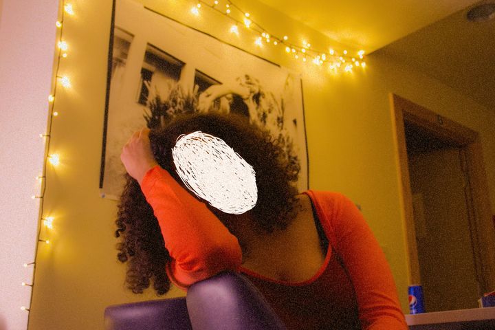 A photo of a woman sitting in a dimly lit room. Her face is scribbled out with white ink