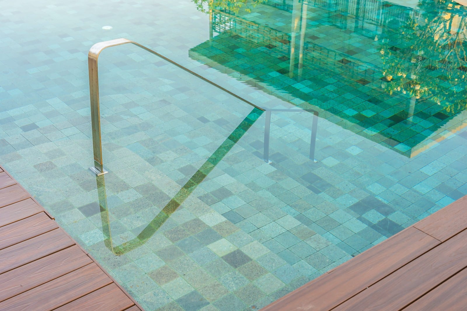 Clean, tiled pool steps with a shiny stainless steel handrail leading into clear water, illustrating why keeping the pool entrance clean is crucial for safety.
